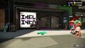 The Headspace shop in Splatoon 2. It sits between Ammo Knights to the right and Shella Fresh to the left. The shop is framed in shiny black metal and supports similar to gutters in the same material, a blackboard with white chalk text sits in front of the left frame. the storefront sits inside of the frame back by a few paces and is sided with dark gray paneling. On the right wall is a black poster with white text and on the left wall are two white papers. On the main wall is a large white glowing sign with the Headspace logo on it in large black text with a thin pink border sitting within the sign along with pink text above the logo and a pink line separating the logo's top and bottom halves which is usually separated by a line of the same color as the text. In front of the sign, there is a table with a hat rack with a Straw Bowler with a black ribbon, the Knitted Hat, and the Hickory Work Cap. On the right side of the door, there is a low rectangular box with an arrow sign propped up out of it by a thin post, the arrow on top being black with white text that points towards the poster on the door which is also in black with white text. The door is framed in black metal and is a wide and shallow pentagon with glass that shows the products inside. The ground is gray and paved.
