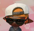 A front view of an Inkling girl with orange ink wearing the Do-Rag, Cap, & Glasses